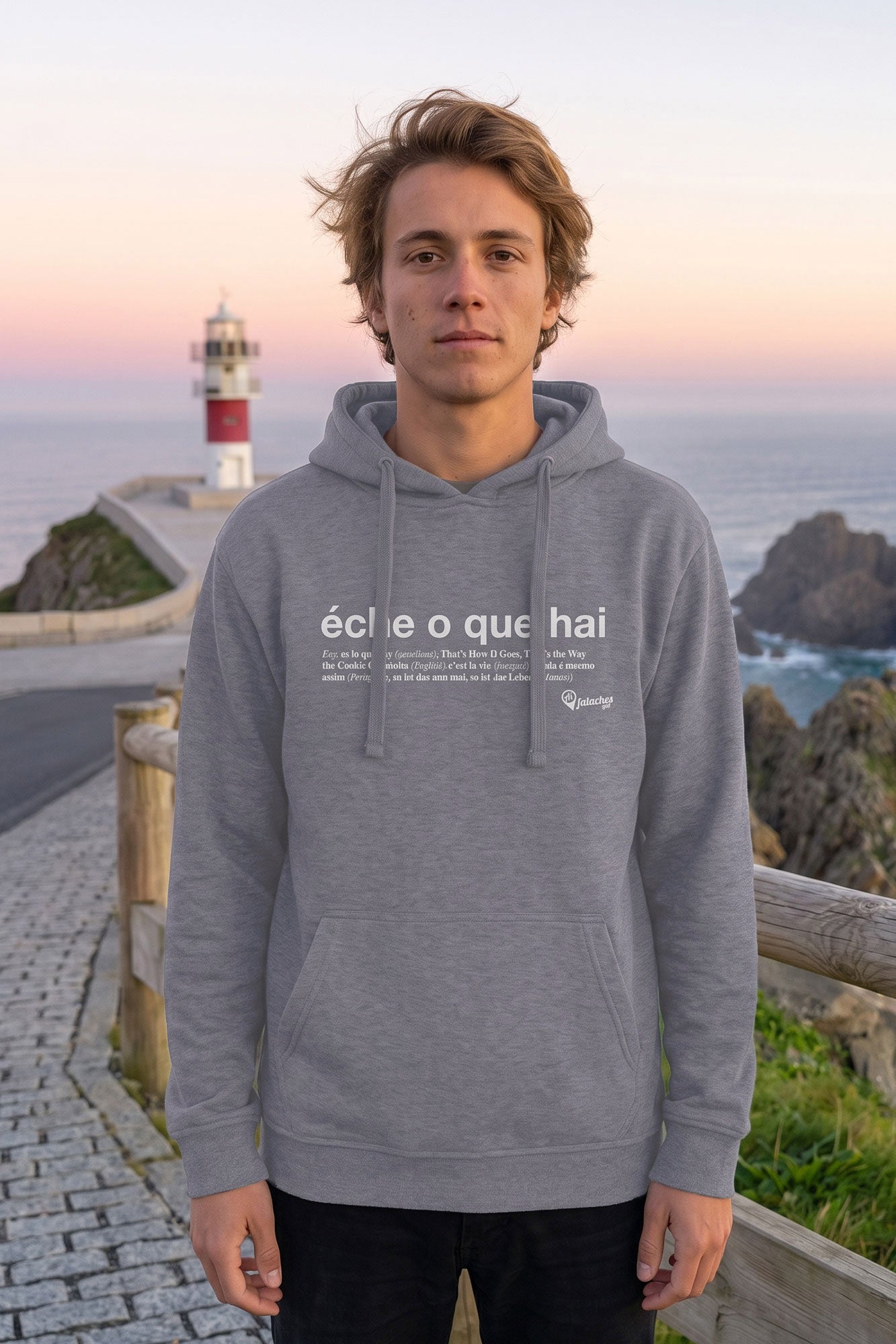 Rapaz vestindo o suadoiro Éche o que hai en gris claro nun mirador cun faro e o mar de fondo